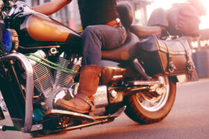 Mann, der auf einem Motorrad fährt, Unteransicht der Beine in Lederstiefeln und Hecktasche hinten am Bike.