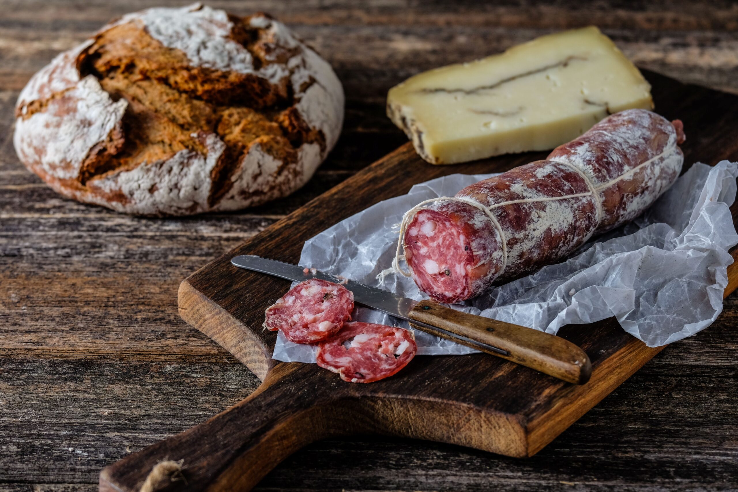 Aufgeschnittene Kaminwurzen auf Holzbrett mit Käse und Bauernbrot
