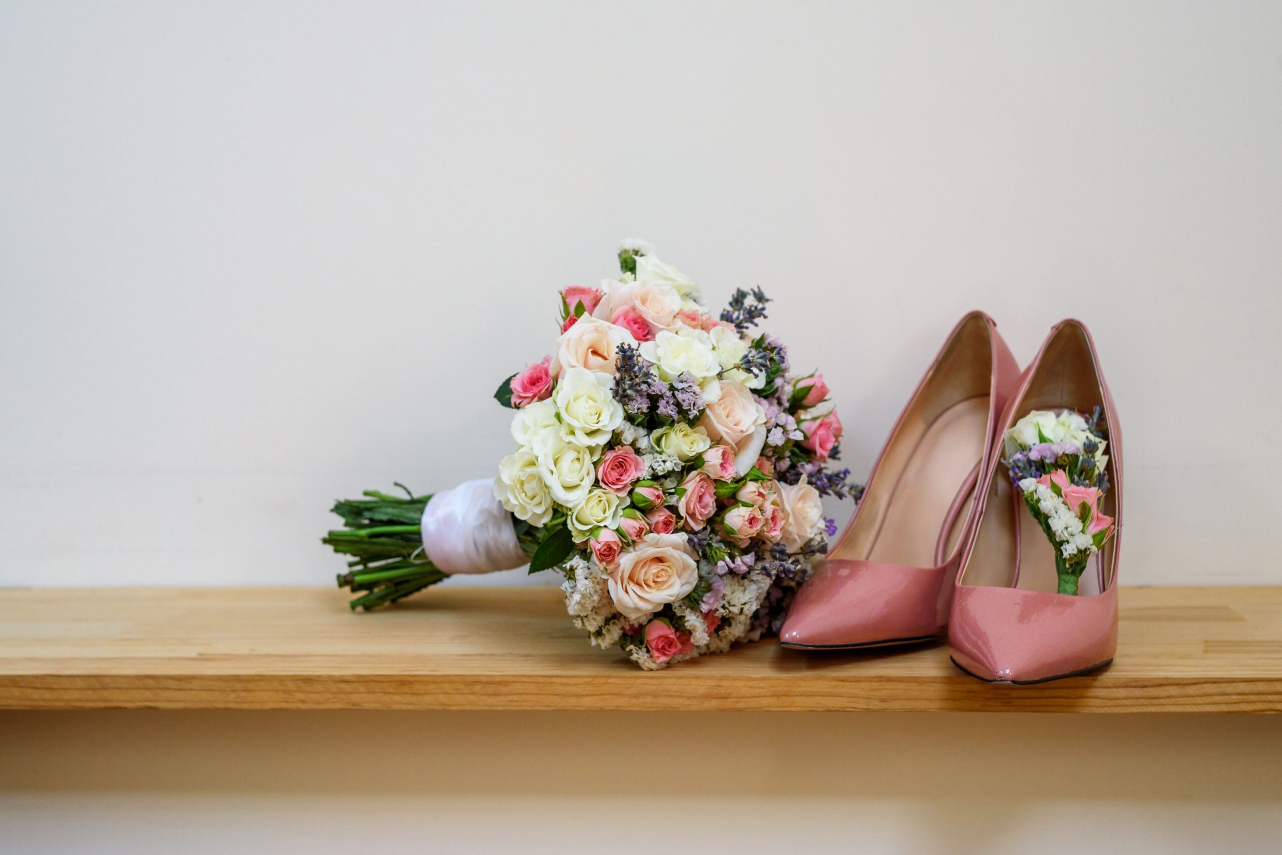 Rosa Brautschuhe mit Blumenstrauß auf Holzbank
