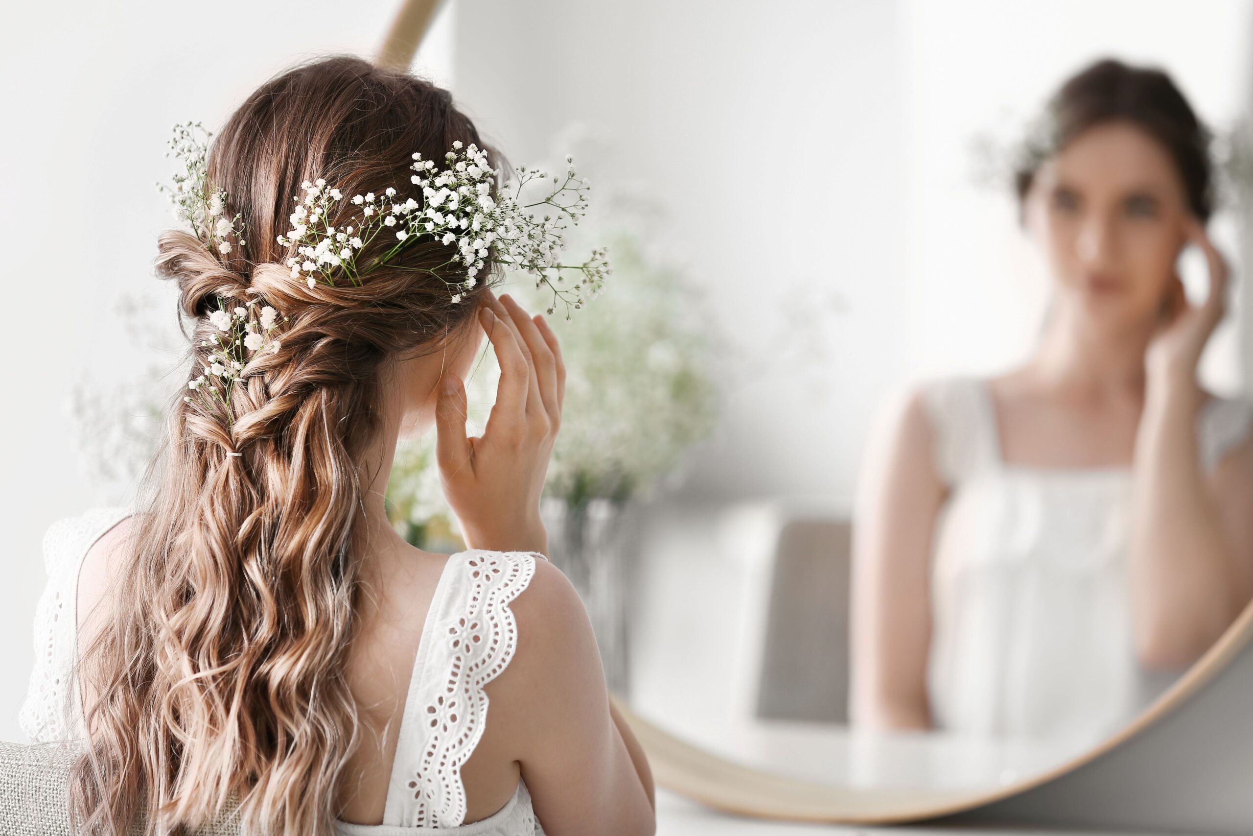 Braut mit Blumenschmuck im Haar blickt in den Spiegel