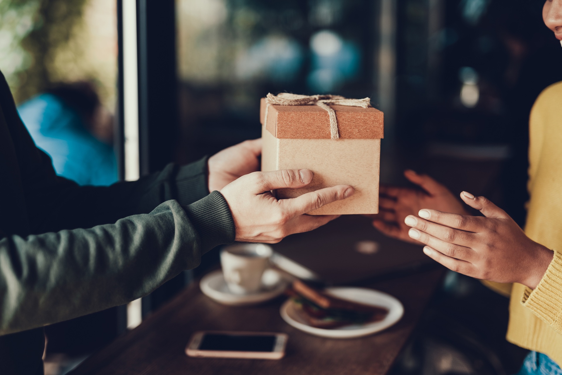 Person überreicht Geschenkbox in gemütlicher Café-Atmosphäre | Bettbank